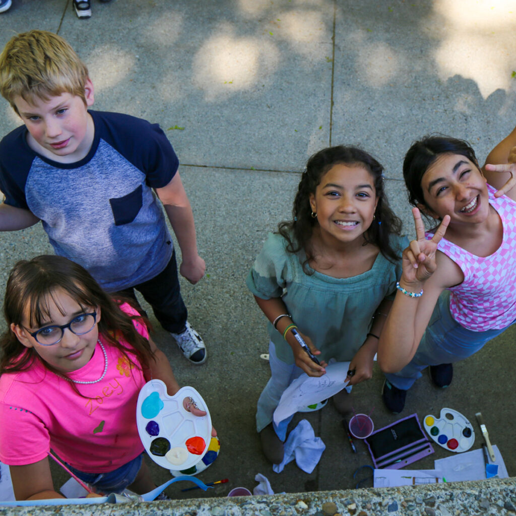 Kids painting on a wall, having fun, and smiling together.